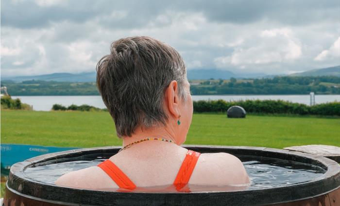 An image of a woman bathing at Halen Môn's Wild Môn Seaweed Baths, bathing in a 40c barrel with views across Eryri.